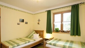 Une chambre avec deux lits en bois, des rideaux verts, une fenêtre donnant sur un beau paysage et une petite lampe fixée au mur.