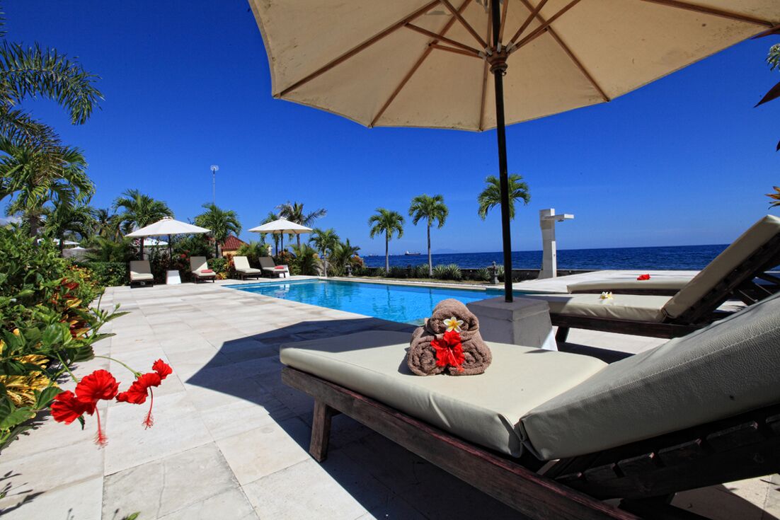 A poolside area with lounge chairs, a pool, and palm trees.