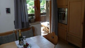 A cozy kitchen with wooden cabinets, a dining table with chairs, and a window with curtains. - Ferienwohnung mit Bergblick (Flintsbach am Inn)