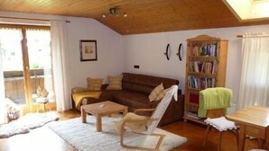 A cozy living room with a brown sofa, a wooden coffee table, a white armchair, and a bookshelf. - Ferienwohnung mit Bergblick (Flintsbach am Inn)