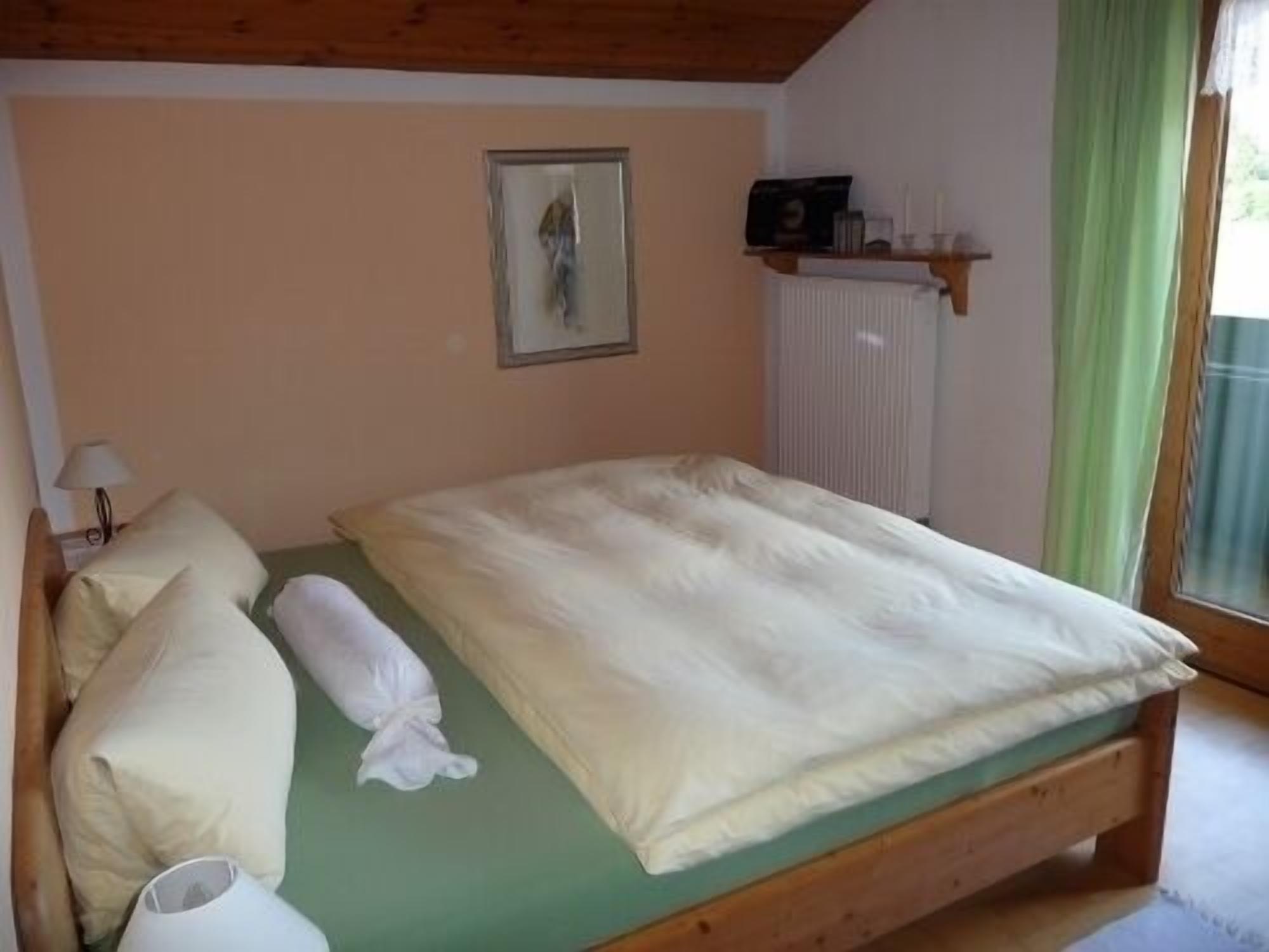Een slaapkamer met een houten bed, een groene matraskap, een kussen, een bedlampje en een ingelijst foto aan de muur.