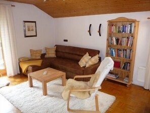 Ein gemütliches Wohnzimmer mit einem braunen Sofa, einem Holztisch, einem weißen Sessel und einem Bücherregal voller Bücher.