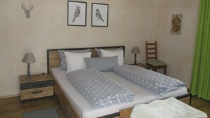 Ein Doppelbett mit gemusterten Betttextilien, zwei Nachttische mit Lampen, ein Sessel und Wandbilder.