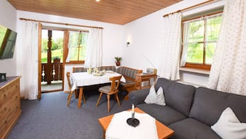 Ein gemütliches Zimmer mit einer Couch, einem Tisch mit Stühlen, einer Holzkommode und einem an der Wand befestigten Fernseher.