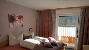 Un dormitorio con cama, mesita de noche, ventana con cortinas y un cuadro en la pared.