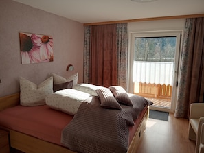A bedroom with a bed, a bedside table, a window with curtains, and a painting on the wall.