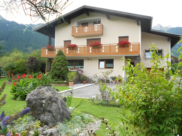 A two-story building with balconies, surrounded by a well-maintained garden with various plants and flowers. - Apartment with 4 edelweiss awarded for 2-4 people in Höfe near Reutte (Höfen)