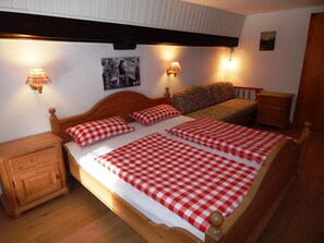 Une chambre à coucher avec un lit en bois, une literie à carreaux, deux lampes de chevet, une table de chevet, un canapé et un tableau accroché au mur.