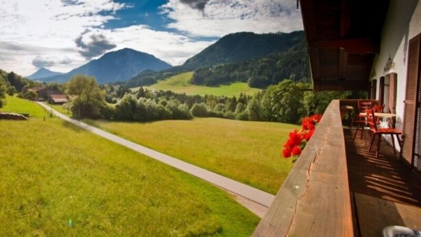 Une terrasse en bois offrant une vue sur un champ verdoyant et des montagnes.