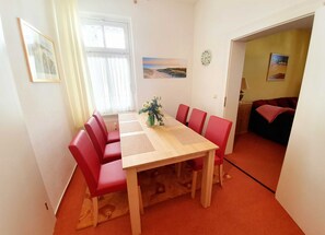 Ruokailutila, jossa on puinen pöytä ja punaiset tuolit, ikkuna, jossa on verhot, seinällä oleva kello ja taulu.