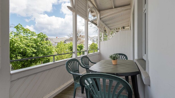 Un balcon abrité, doté d’une table et de chaises, qui offre une vue sur un paysage verdoyant et luxuriant.