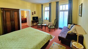 Une chambre d’hôtel avec un grand lit, un canapé, un bureau avec une chaise, une télévision et une fenêtre avec des rideaux.