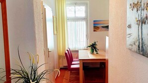 Un coin repas comprenant une table, des chaises, un vase avec des fleurs et une fenêtre avec des rideaux.