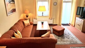 Un salon avec un canapé, une table basse, une lampe, un téléviseur et une fenêtre avec des rideaux.