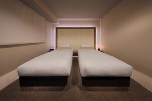 A hotel room with two single beds, a large padded headboard, and a carpeted floor.
