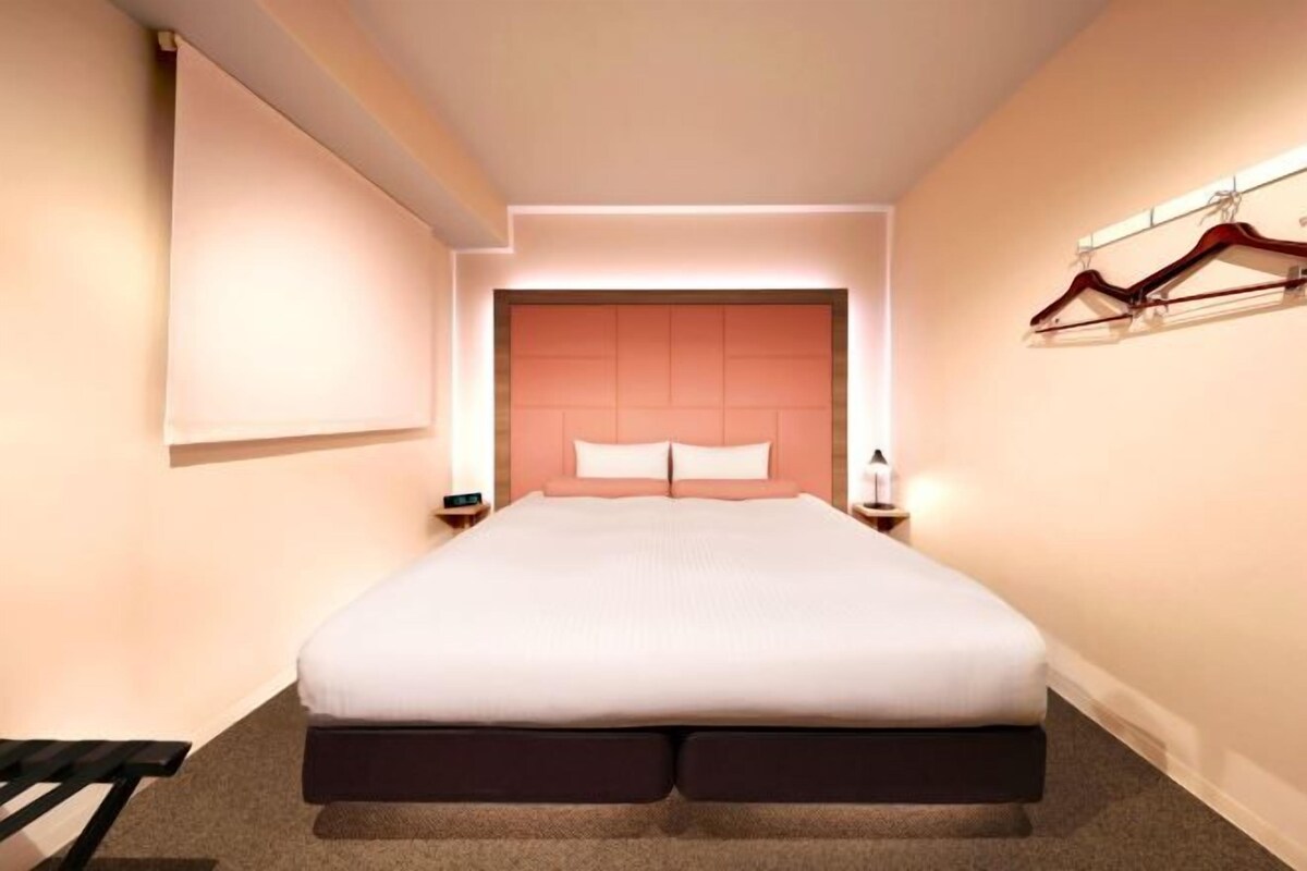 Una habitación de hotel moderna con una cama grande, mesitas de noche y un armario con ropa colgada.