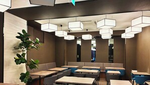 A modern restaurant interior with multiple seating areas, including booths and tables, and a large potted plant. - Doutonbori Crystal Hotel (Osaka)