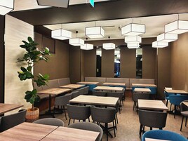 A modern restaurant interior with multiple seating areas, including booths and tables, and a large potted plant.