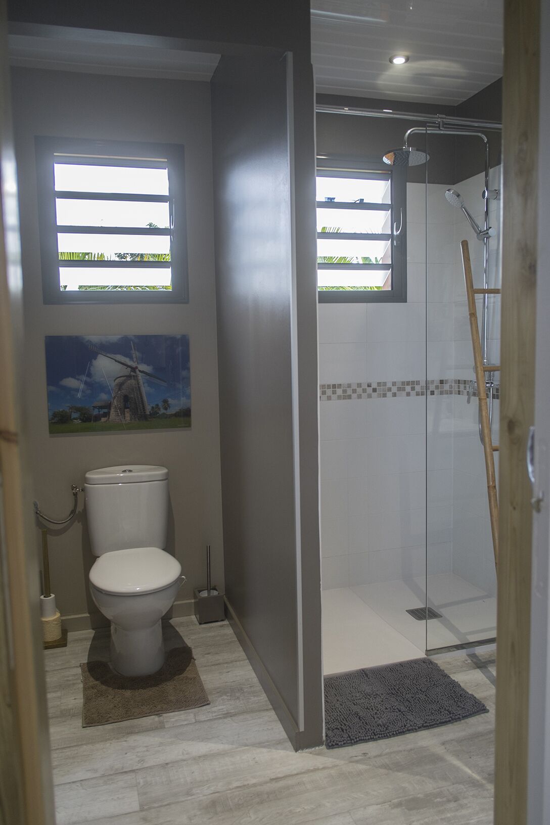 Une salle de bain avec des toilettes, une douche et une fenêtre donnant sur un espace verdoyant.