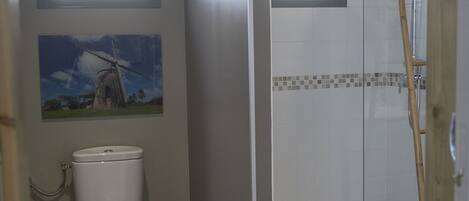 Une salle de bain avec des toilettes, une douche et une fenêtre donnant sur un espace verdoyant.