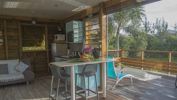 Une terrasse en bois comprenant un coin repas, un canapé et une cuisine équipée d’un four à micro-ondes et d’un évier.