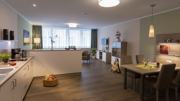 Eine moderne Küche mit Kochinsel, ein Essbereich mit Tisch und Stühlen sowie ein Wohnbereich mit Sofa und Fernseher.