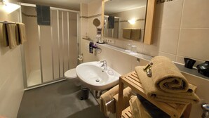 Un baño con lavamanos, espejo, toallero y ducha.