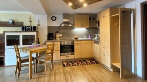 Cocina compacta con armarios de madera, horno integrado y comedor con mesa y sillas de madera.