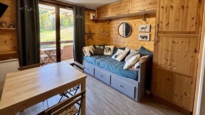 Una cabaña acogedora con interior de madera, una cama con muchas almohadas, una mesa de comedor y un ventanal corredero que da a un espacio exterior.