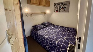 Un dormitorio pequeño con una cama individual, un armario de madera sobre la cama y una lámpara fijada a la pared.
