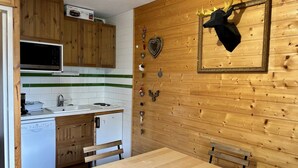Cocina compacta con armarios de madera, microondas, lavavajillas y una mesa de comedor con dos sillas.