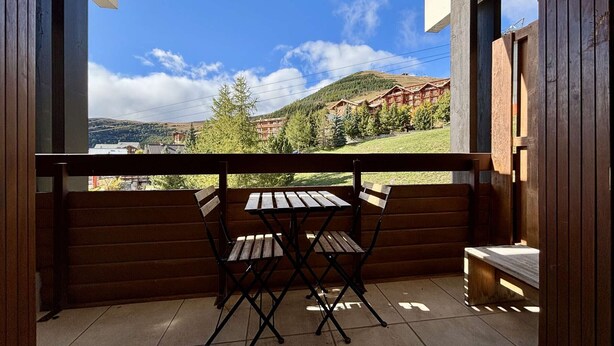 Un balcón con mesa y sillas de madera, con vista a una zona montañosa con edificios.