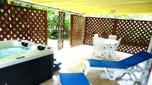 A hot tub, lounge chairs, and a table in a covered outdoor area with a wooden lattice fence. - Lecres St Ange Elie Gites with Spa (lamentin)