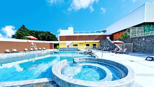 A swimming pool with lounge chairs and a hot tub, surrounded by stone walls and a building with a modern design. - Lecres St Ange Elie Gites with Spa (lamentin)