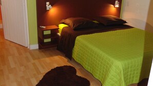 A bedroom with a bed, nightstands, a green quilted bedspread, a brown rug, and a wall with a Buddha image. - Lecres St Ange Elie Gites with Spa (lamentin)