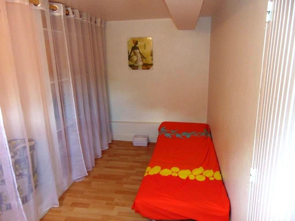 Ein kleines Zimmer mit einem Bett, einem Fenster mit durchsichtigen Vorhängen und einem Bild an der Wand.