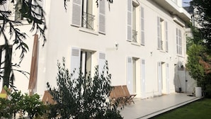Ein weißes Gebäude mit zahlreichen Fenstern und Türen, umgeben von einem gepflegten Rasen und Kübelpflanzen.