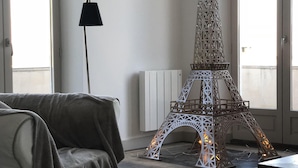 Ein Zimmer mit großem Fenster, einer Couch, einer Lampe und einem dekorativen Eiffelturm-Modell.