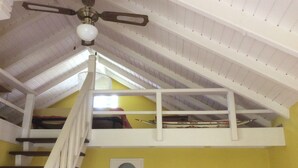 Ein Zimmer mit hoher Decke, einer weißen Treppe und einem Deckenventilator.