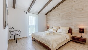 Une chambre avec un plancher en bois, un lit recouvert de draps blancs, une table de chevet avec une lampe et une chaise.