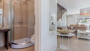 Une salle de bain moderne avec une douche à parois de verre, des toilettes et un lavabo. On y trouve également un espace de vie avec un canapé, une table basse et un escalier menant à l’étage supérieur.