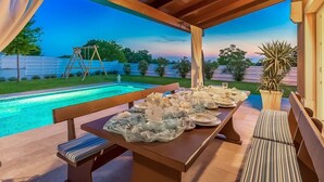 Un espace de restauration en plein air avec vue sur la piscine, des bancs en bois et une table dressée pour un repas.