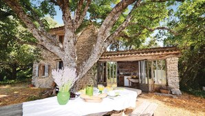 An outdoor dining area with a table set for two, surrounded by stone walls and a large tree. - 1 bedroom beautiful home in Saignon (Saignon)