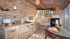 A rustic kitchen with stone walls, wooden cabinets, a stone countertop, a wooden table with a hat and fruit bowl, and a hanging basket. - 1 bedroom beautiful home in Saignon (Saignon)