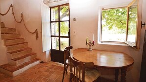 A room with a wooden staircase, a round wooden table with chairs, and two windows with views of greenery. - 1 bedroom beautiful home in Saignon (Saignon)