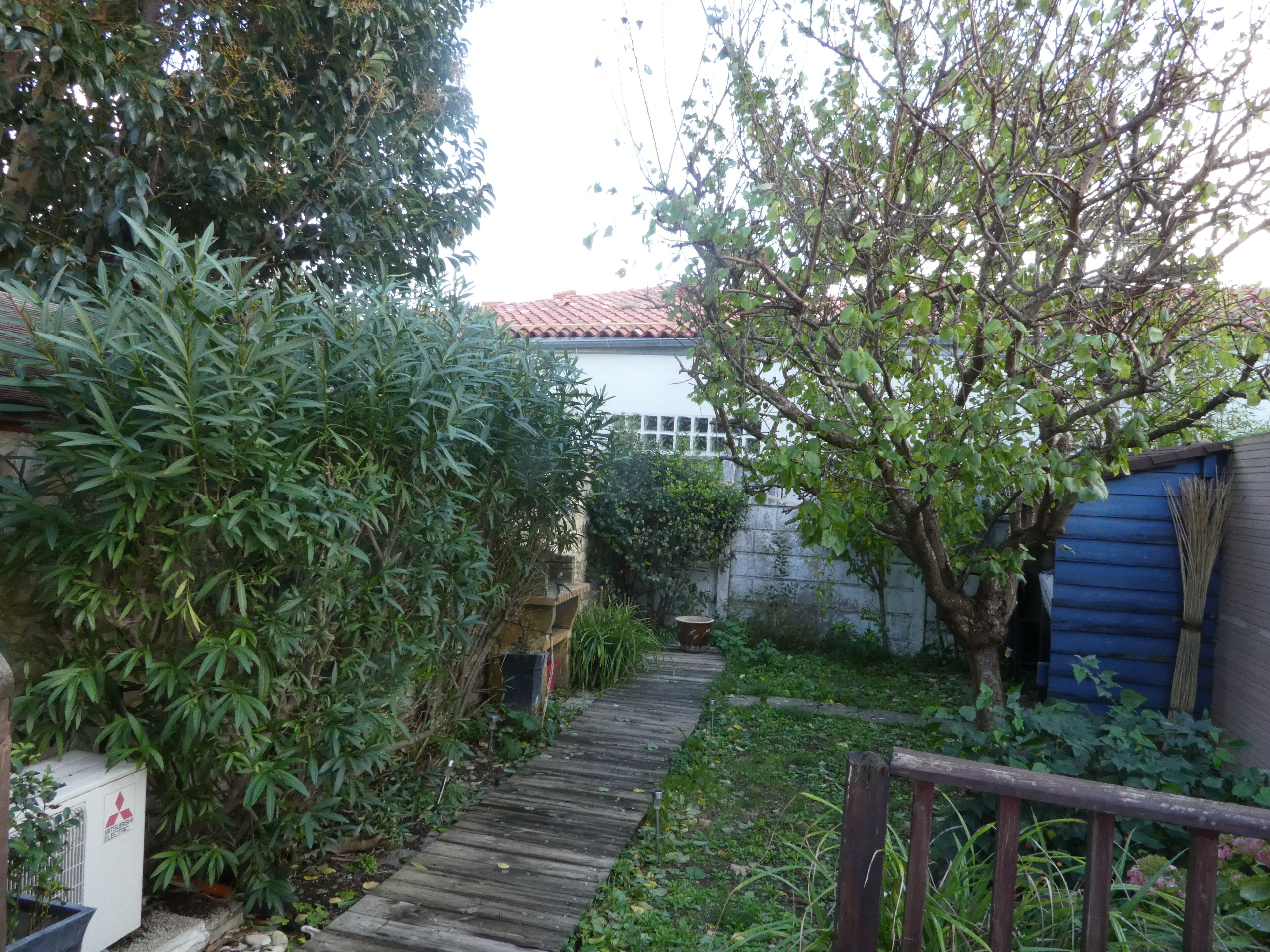A narrow wooden pathway leading to a house with a tiled roof.