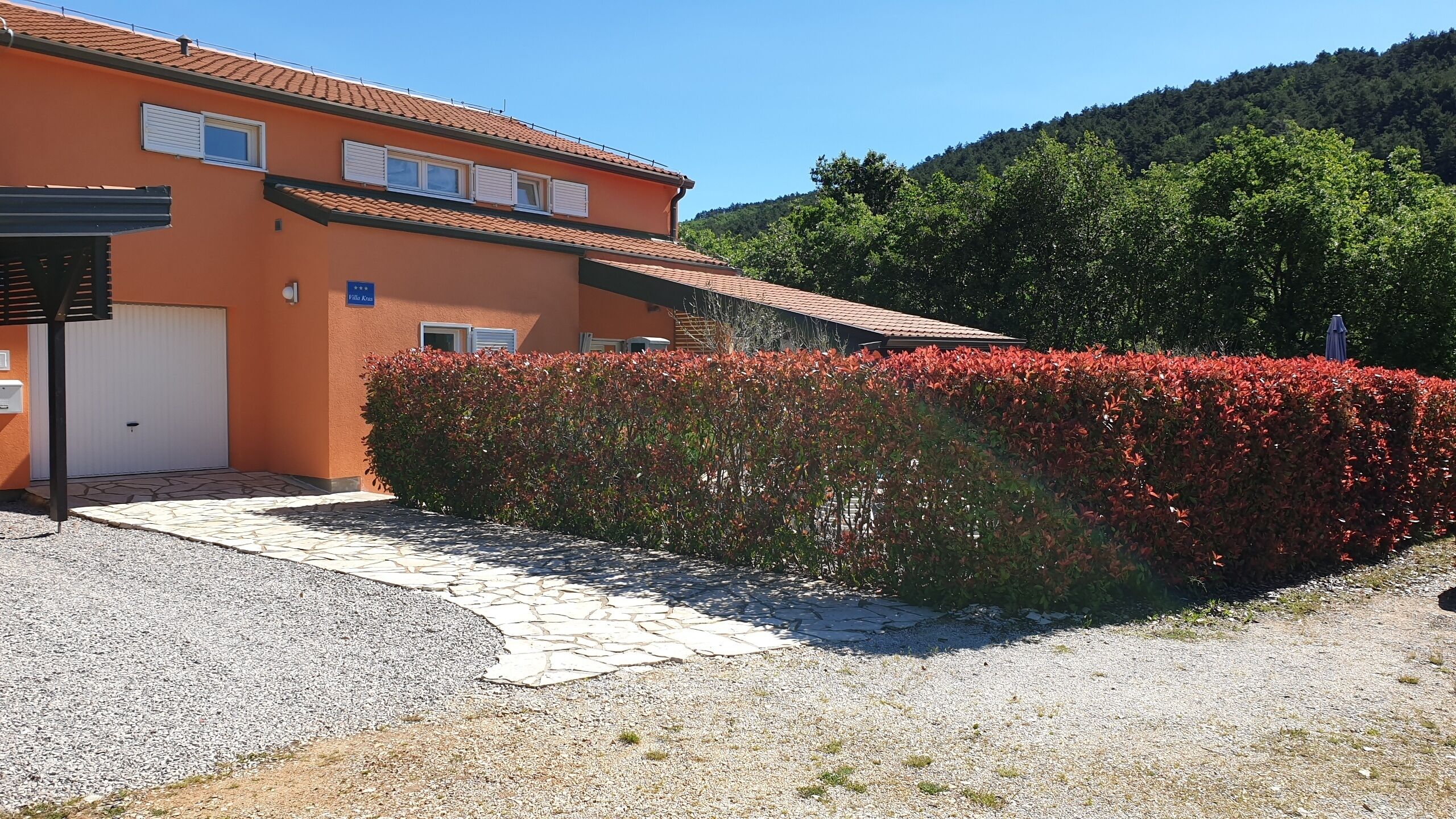 A two-story building with a tiled roof, a gravel driveway, and a well-maintained hedge.