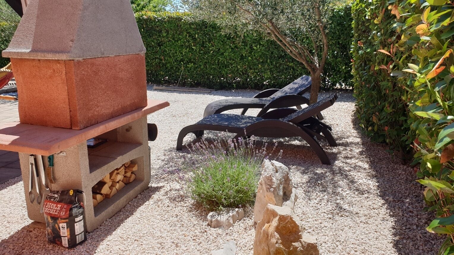 An outdoor grill area with a stone chimney, a bench, and a bag of charcoal.