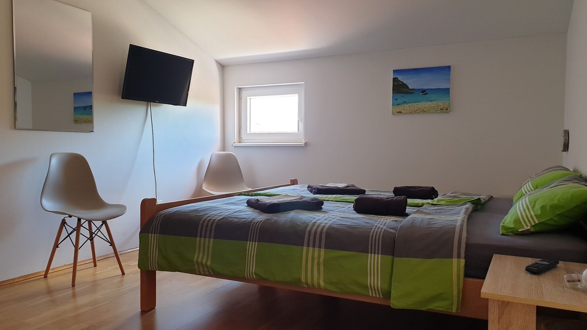 A bedroom with a bed, two chairs, a TV, a window, and a painting.