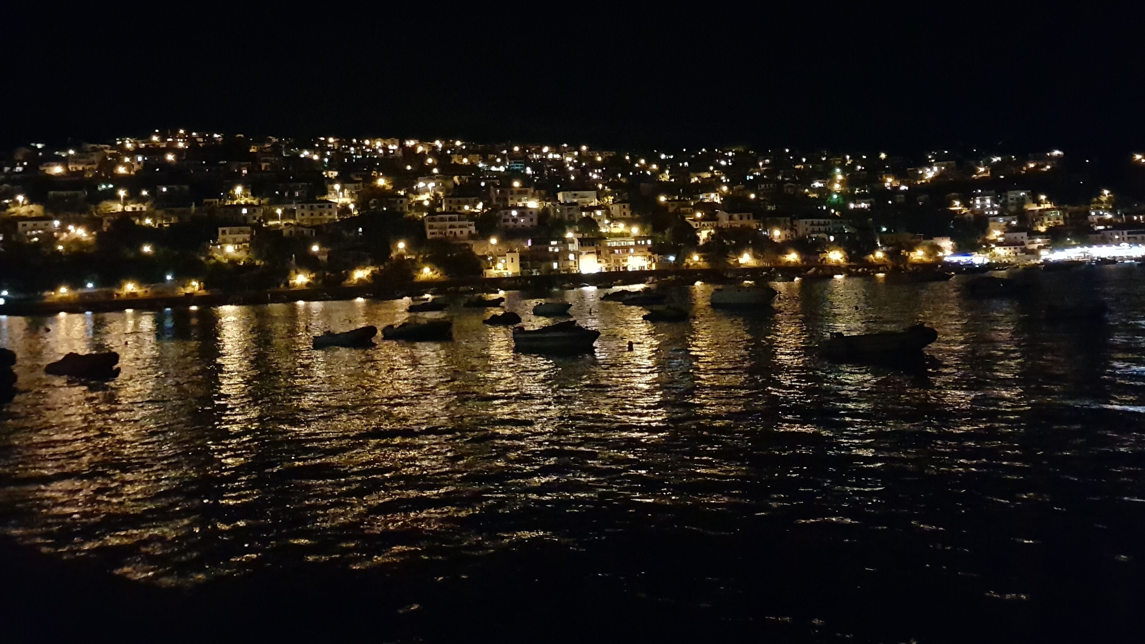 A nighttime view of a cityscape with buildings illuminated by streetlights, reflecting on the water.